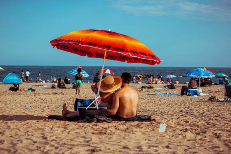 People sitting under a beach umbrella on a sunny day, practicing sun protection.