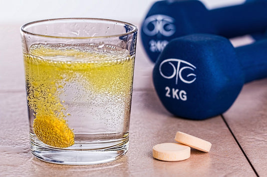 A glass of water beside two tablets and dumbels.